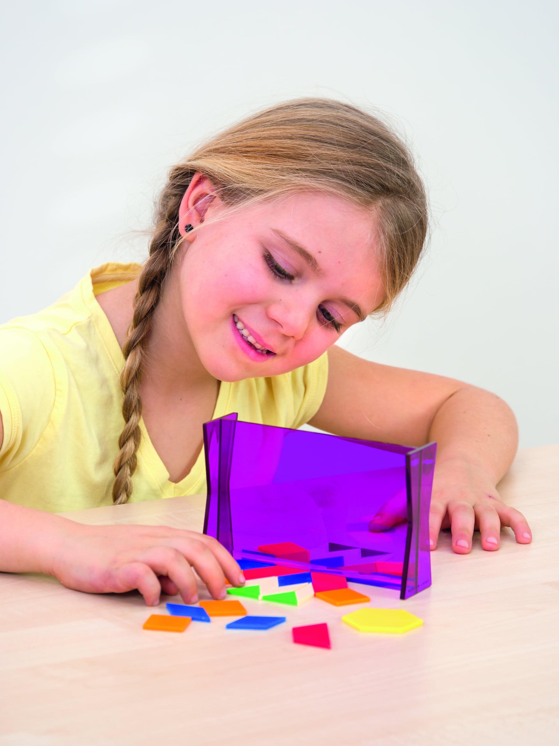 Meisje met vlechten speelt met een paarse geometrie toverspiegel en kleurrijke vormen op een tafel.