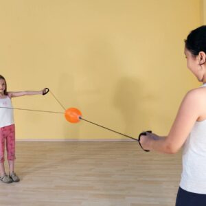 Swoosh bal in gebruik door twee kinderen, met handvatten en een oranje bal, tegen een gele muur.