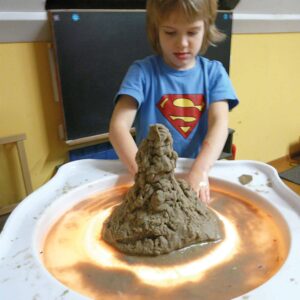 Kinderen experimenteren met kleur en licht op een ronde lichttafel met een zandvorm in het midden.