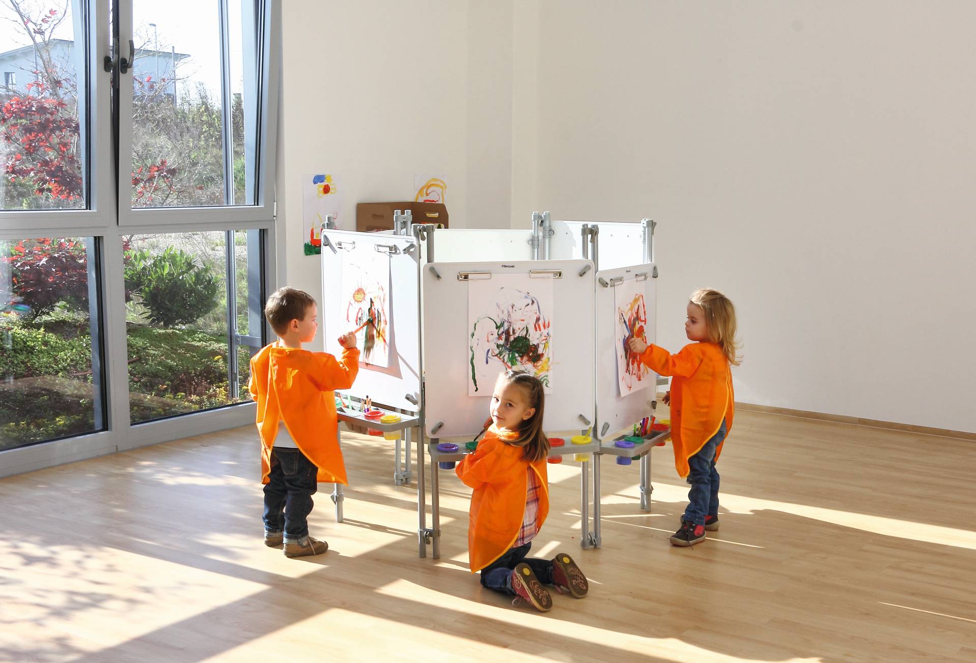 Teken-/schilderwand 6-zijdig met kinderen in oranje schorten die creatief aan het werk zijn in een lichte ruimte.