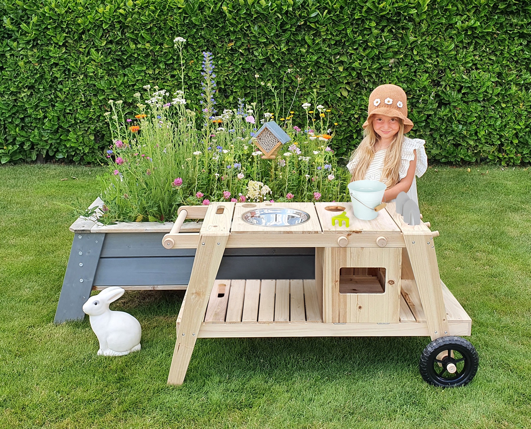 Houten Knoeikeuken met speelruimte, plantenbak en accessoires, gebruikt door een meisje in een hoed in de tuin.