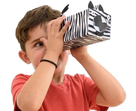 Jongen met een zelfgemaakte telescoop in zebra-stijl, kijkend door het kijkgat, creatief knutselmateriaal zichtbaar.