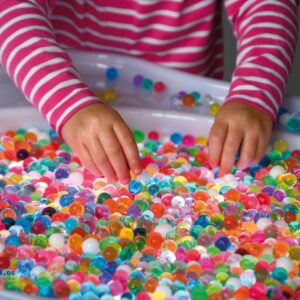 Kleurrijke Sensori Aqua Gel Parels in een speeltafel, met handen die de parels aanraken en verkennen.