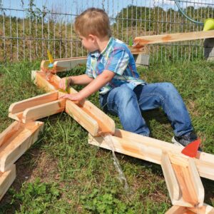 Stevige houten waterbaan met een jongen die speelt, water stroomt door de zelfgebouwde waterweg in de tuin.