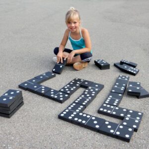 Meisje speelt met grote, zachte dominostenen op de grond, met een domino-opstelling en extra stenen ernaast.