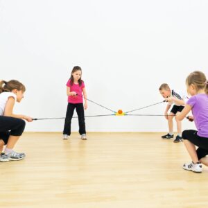 Kinderen oefenen hun evenwicht en coördinatie met een balanceerbord aan elastieken in een lichte ruimte.