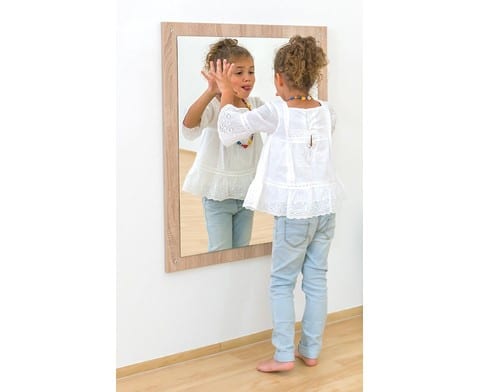 Rechthoekige eiken spiegel met houten lijst, een meisje in witte blouse kijkt en speelt voor de spiegel in een lichte ruimte.
