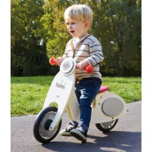 Stijlvolle loopfiets Vespa met rode handvatten, gebruikt door een kind op een pad in een groene omgeving.