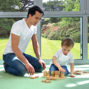 Houten Montessori vormen en puzzels, gebruikt door een volwassene en een kind op een groene vloer, met natuur op de achter...