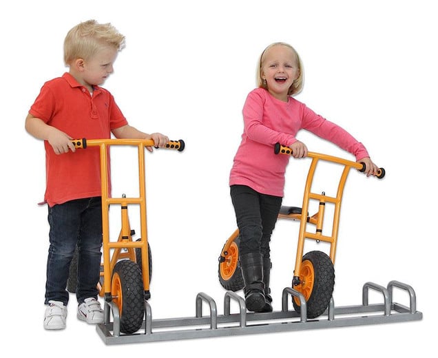 Twee kinderen met loopfietsen bij een metalen fietsenhok voor school, ideaal voor buitenspelen en kinderopvang.
