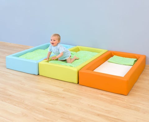Comfortabel schuimbedje in blauw, groen en oranje, met een kind dat erop kruipt, ideaal voor kinderopvang en peuterruimtes.
