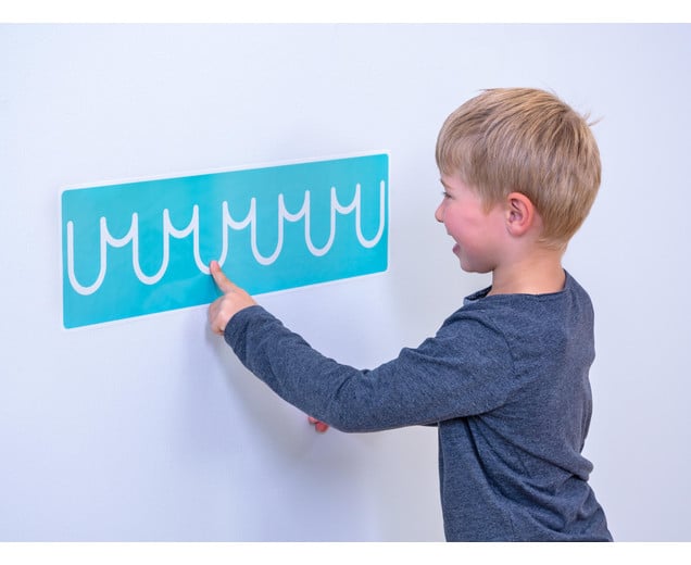 Jongen wijst naar een turquoise oefenbord met golvende lijnen voor schrijfvaardigheidsoefeningen.