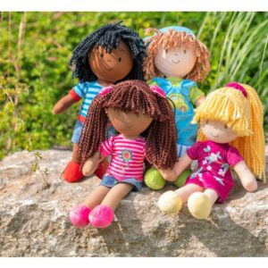 Set van vier kleurrijke stoffen poppen met verschillende kapsels en outfits, zittend op een steen in de natuur.