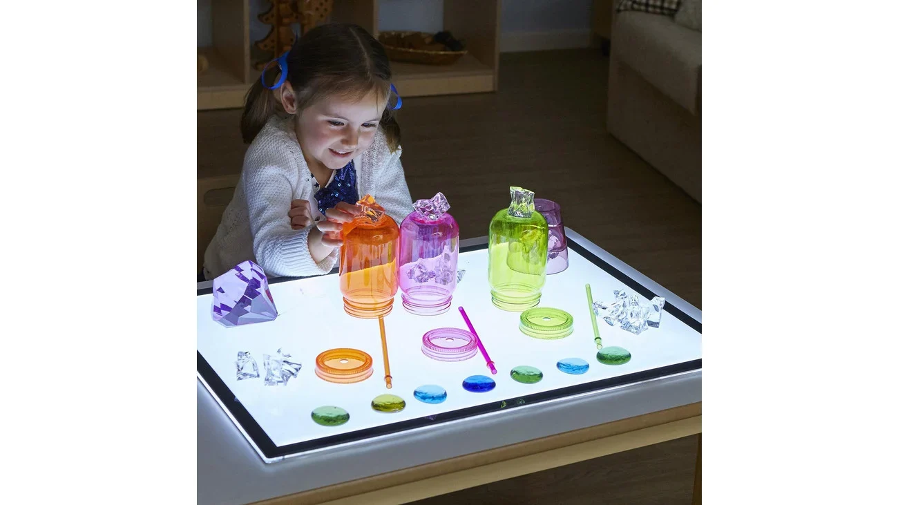 Lichttafel A2 met kleurrijke transparante flessen en objecten, gebruikt door een kind voor speelse lichtexperimenten.