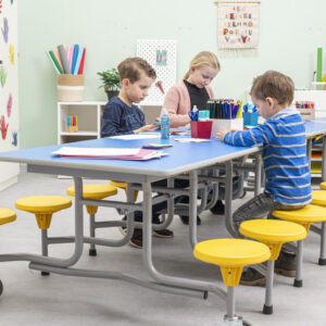 Vouwtafel met blauwe tafelblad en gele krukken, gebruikt door kinderen in een klaslokaal. Tafelhoogte 61 cm.