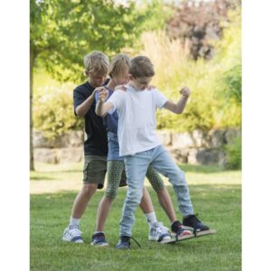 Drie kinderen spelen samen op zomerskis op gras, lachend en in beweging, met een groene achtergrond.