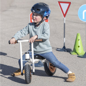 Kindje rijdt op de robuuste loopfiets Tiny Walker met een helm, omringd door verkeersborden en kegels.