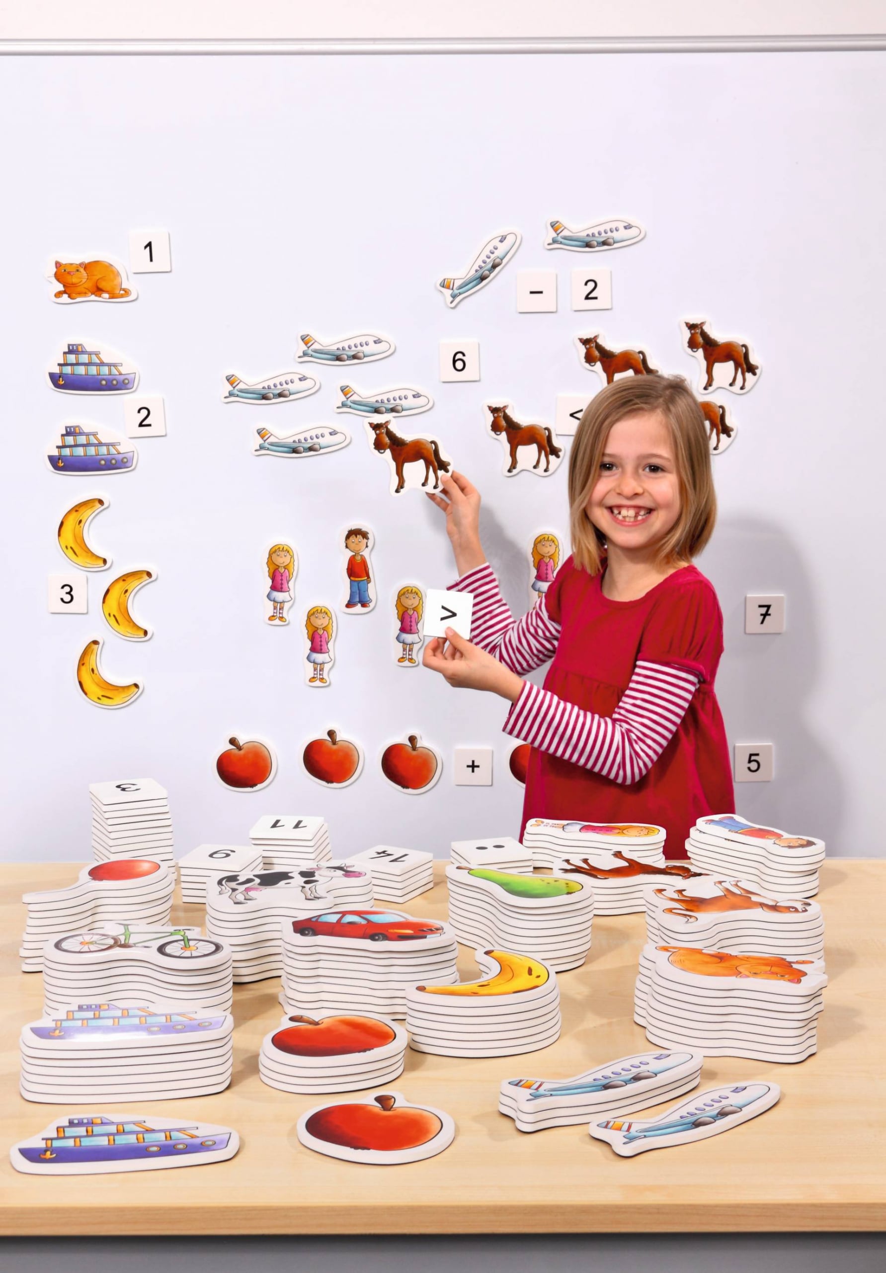 Magnetische rekenplaatjes met dieren, voertuigen en fruit, gebruikt door een kind op een bord voor rekenactiviteiten.
