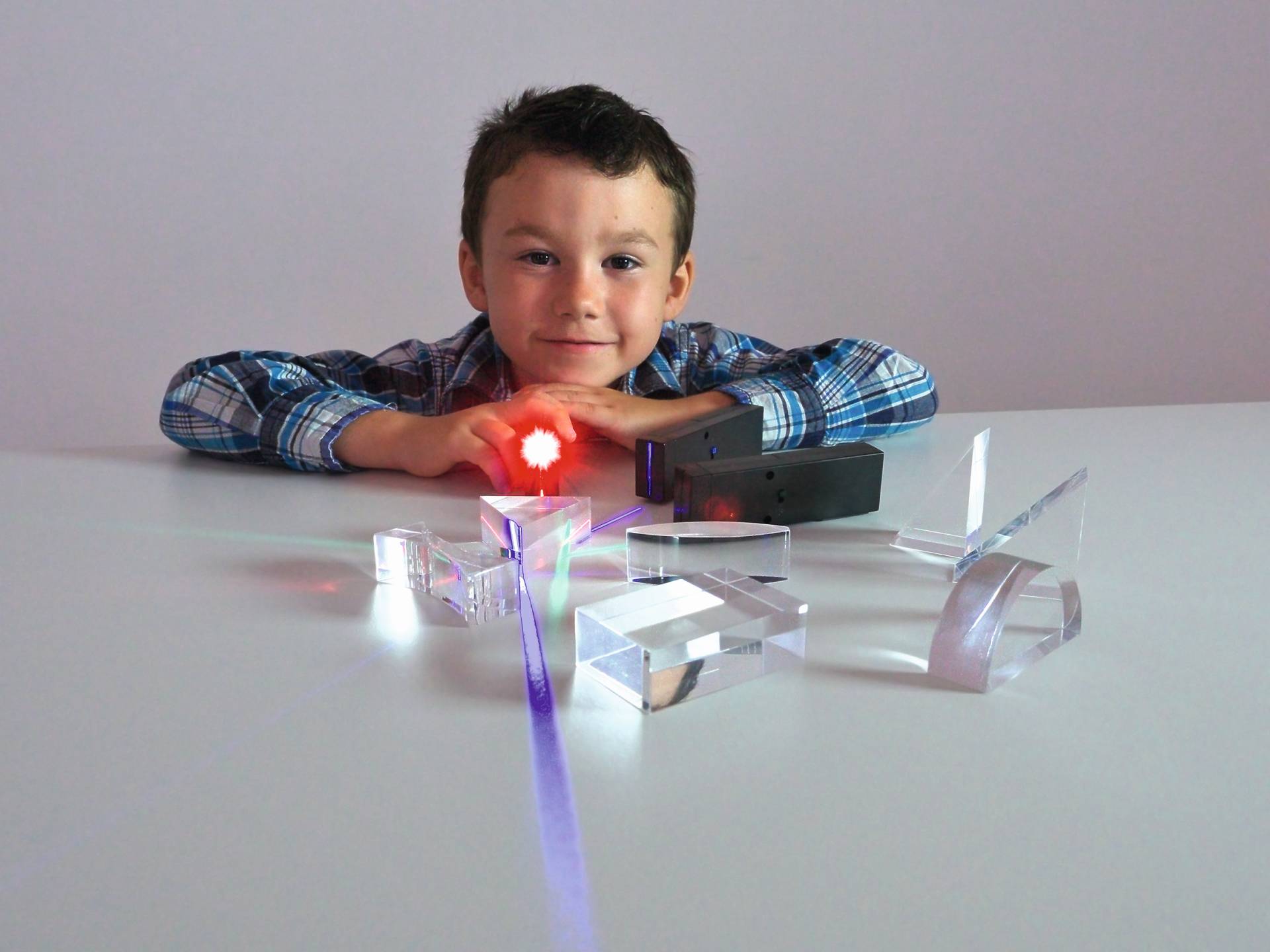Kind met LED-kleurenlampen en transparante objecten, experimenteert met licht en kleur op een tafel.