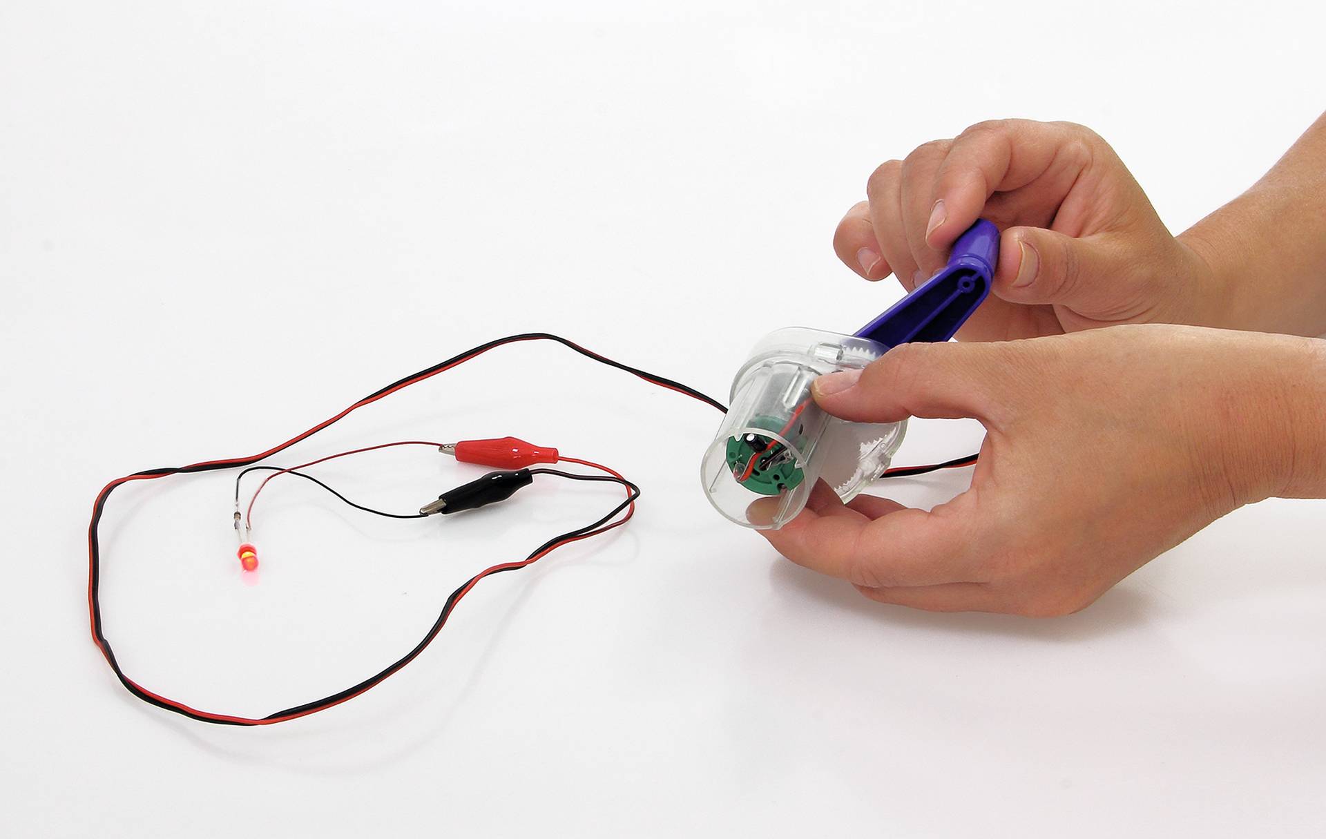 Dynamo met handvat, draden en LED-lampje; toont omzetting van beweging in elektriciteit.