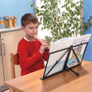 Tafelstandaard voor muzieknoten met bladmuziek, gebruikt door een jongen die op een blokfluit speelt, in een klaslokaal.