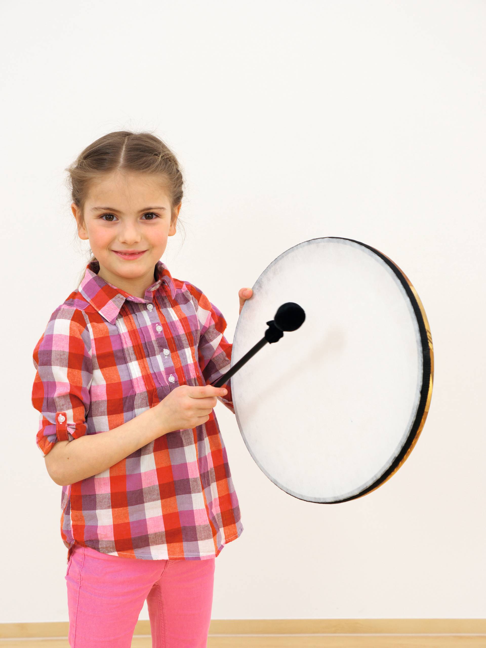 Meisje in een geruit shirt houdt een framedrum vast, klaar om te spelen met een stok. Geschikt voor jonge kinderen.