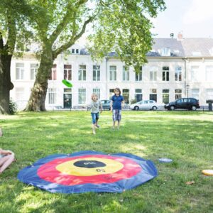 Kinderen spelen frisbee dart in het park, met een groot dartbord op de grond en frisbees in de hand.