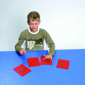 Kind met tastkaarten van hoofdletters, rode kaarten met gouden letters, zittend aan een blauwe tafel.