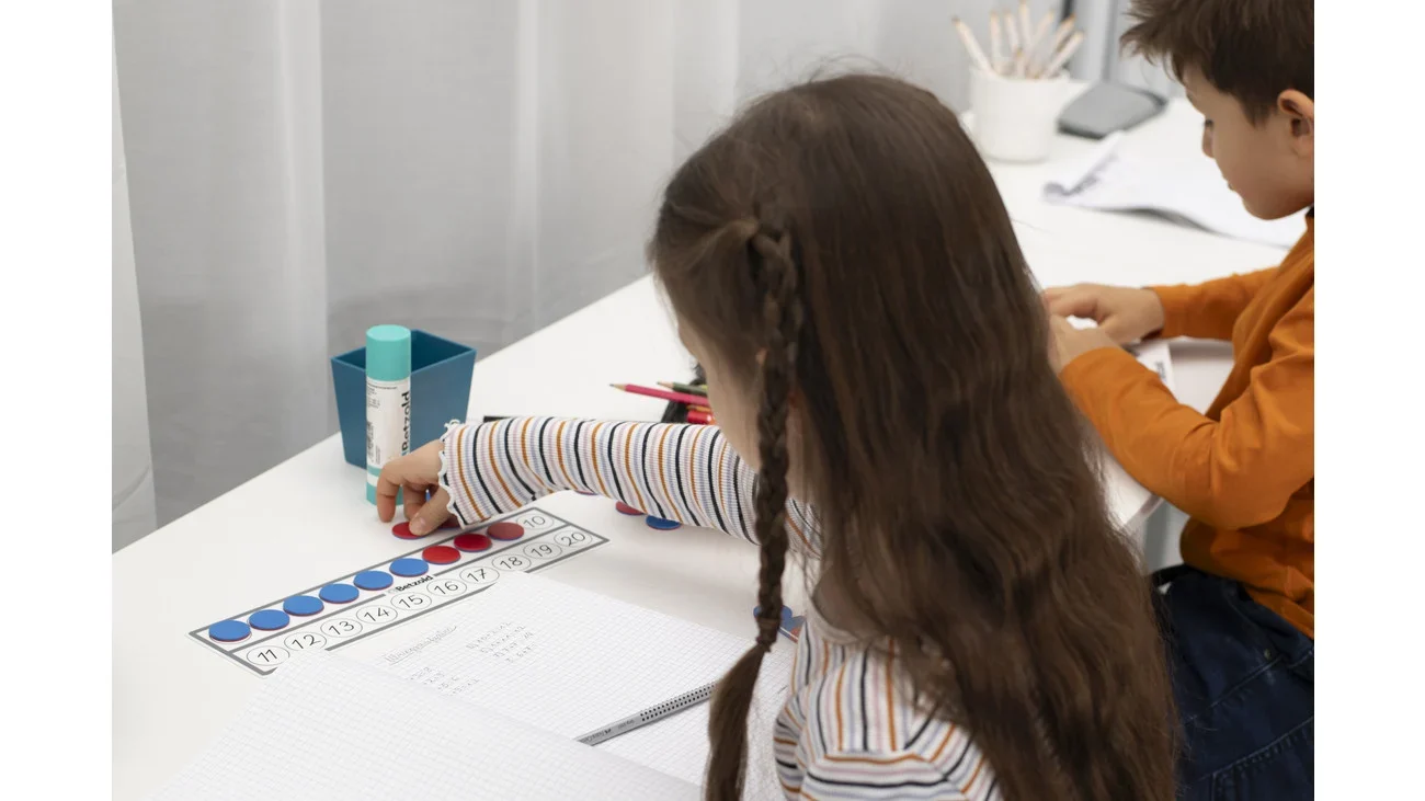 Drie omkeerbare tegels in gebruik, kinderen rekenen met blauwe en rode fiches op een bureau met schrijfmateriaal.