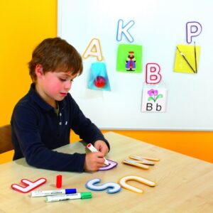 Kleurrijke plastic letters van 11,5 cm, set van 26, gebruikt door een jongen voor schrijfactiviteiten op een tafel.