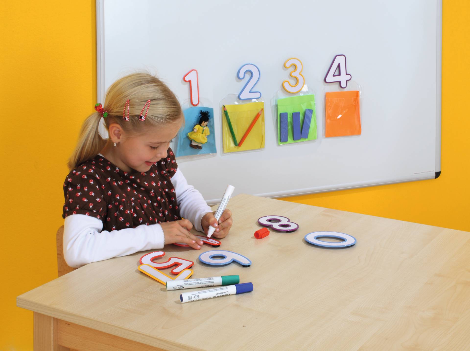 Magnetische beschrijfbare letters in verschillende kleuren, met een kind dat ze aan het schrijven is aan een houten tafel.