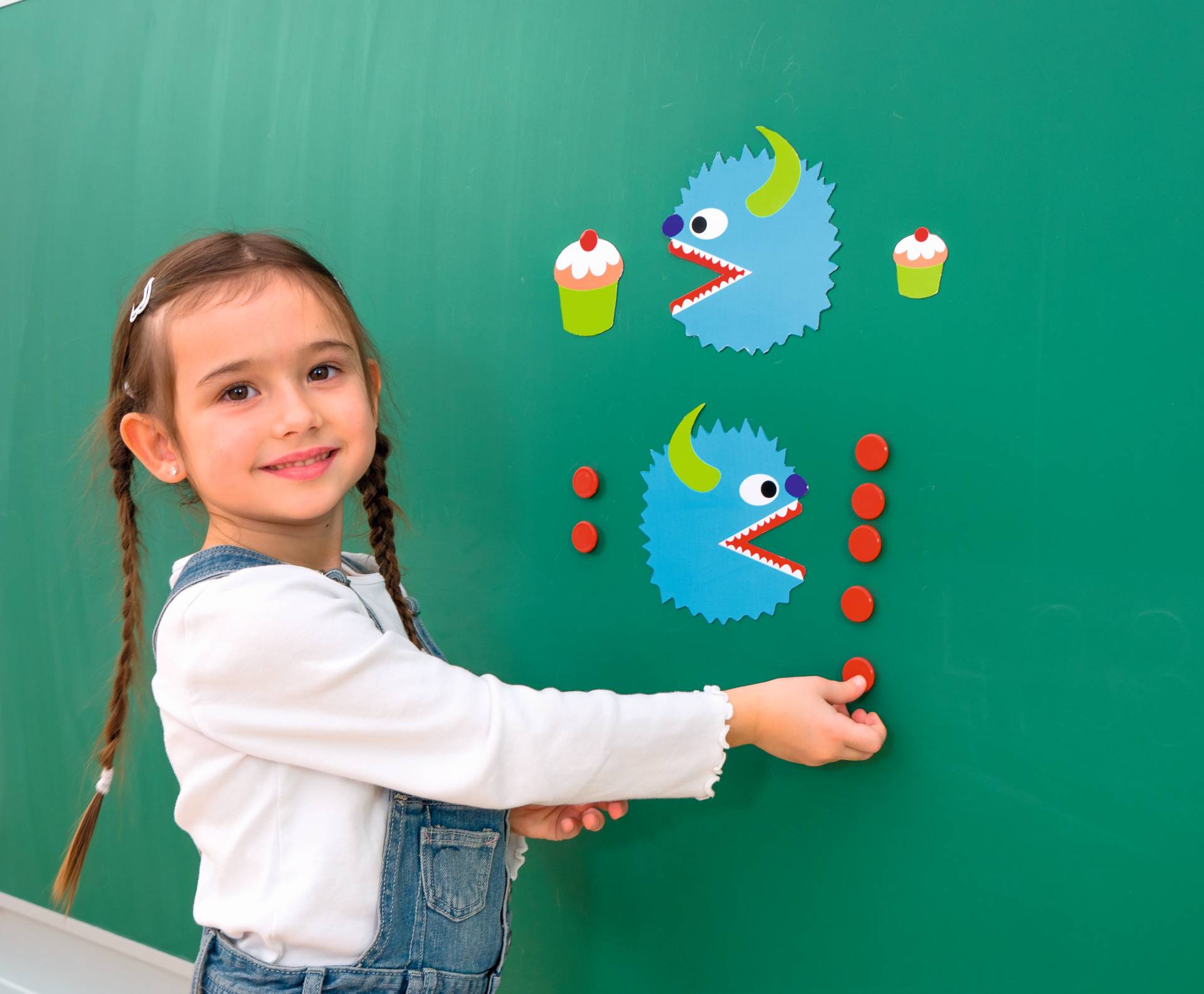 Magnetische rekenmonsters op een schoolbord, een meisje plaatst cijfers en monsters voor optellen en aftrekken.