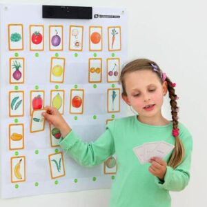 Interactieve leerwand met kleurrijke afbeeldingen van groenten en fruit, gebruikt door een kind met kaarten.