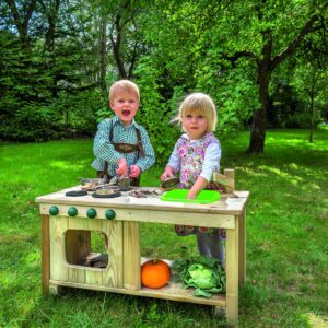 Peuter buiten keuken van hout met twee kinderen die spelen, koken met speelgoedkeukengerei en groenten in een groene tuin.