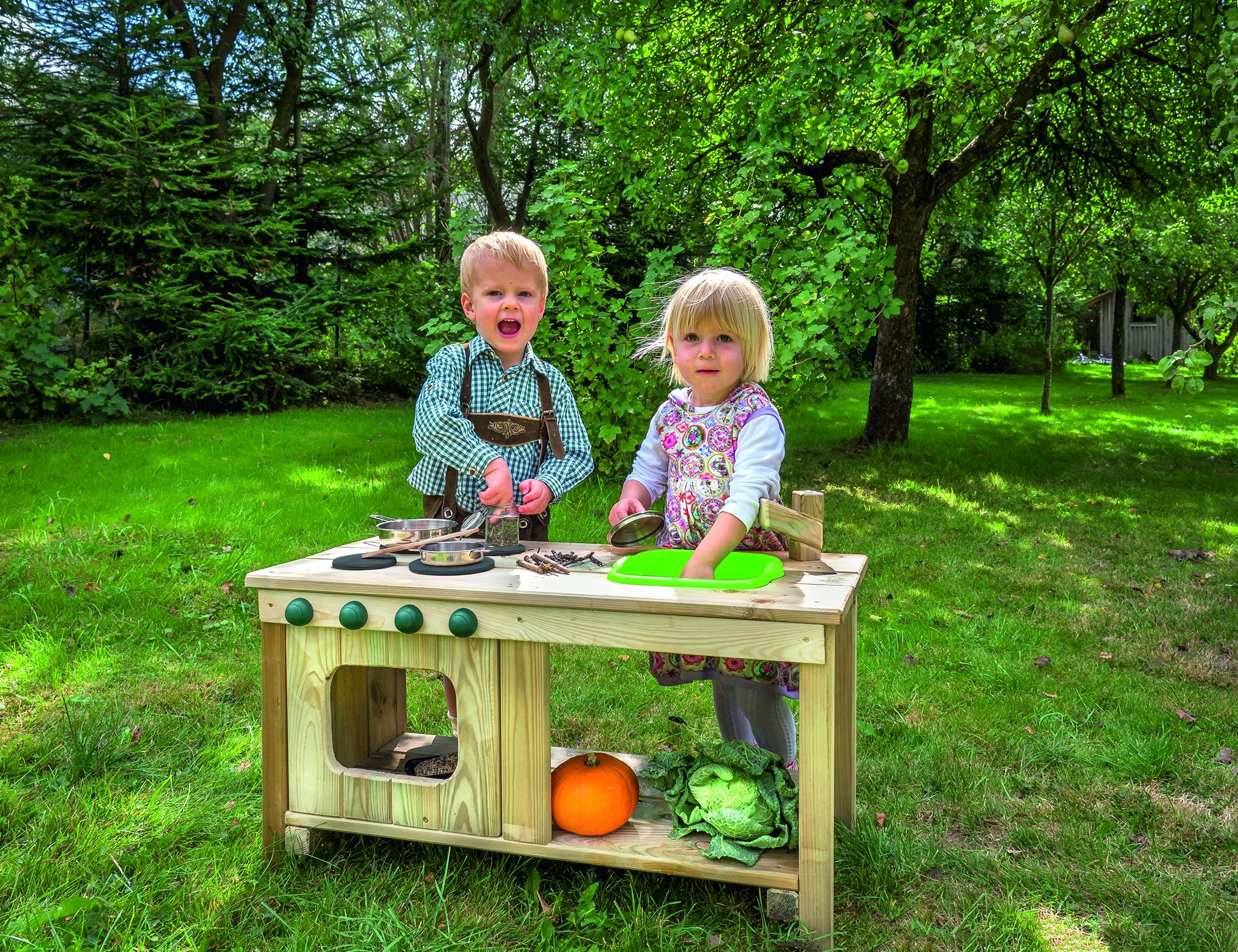 Peuter buiten keuken van hout met twee kinderen die spelen, koken met speelgoedkeukengerei en groenten in een groene tuin.