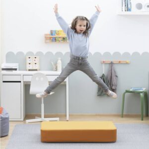 Een kind springt vrolijk op een geel indoor springkussen in een speelse, lichte kamer met meubels en decor.