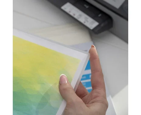 Lamineerfolie A4, mat en glanzend, 150 mic, stevig, met kleurrijke afdrukken in de hand, printer op de achtergrond.