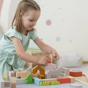 Meisje speelt met kleurrijke houten blokken op een tafel, bouwend aan een speelwereld met verschillende vormen en figuren.