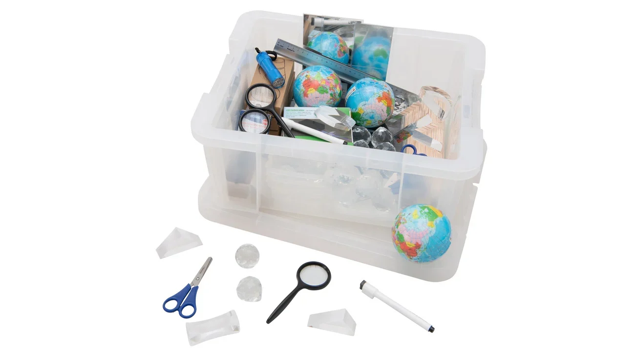 Transparante doos met diverse optische materialen zoals lenzen, spiegels, globes en meetinstrumenten voor lichtexperimenten.