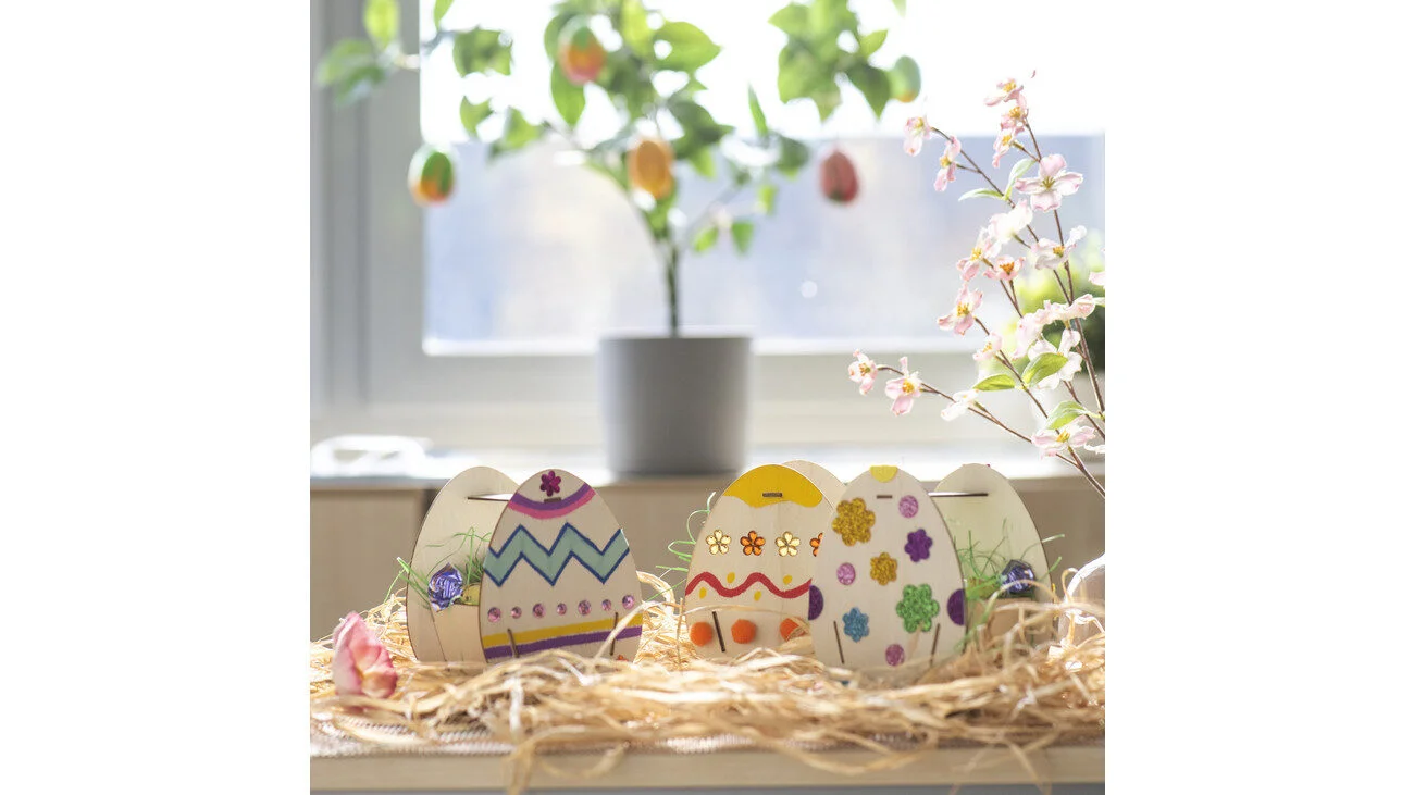 Set van 6 houten paasmandjes in ei-vorm, versierd met kleurrijke patronen en bloemen, op een tafel met planten.