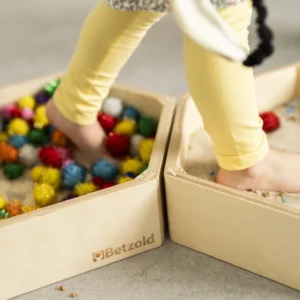 Kindervoeten op zachte balletjes en in fijn zand, in een houten speelset voor motorische ontwikkeling en zintuiglijke ontd...