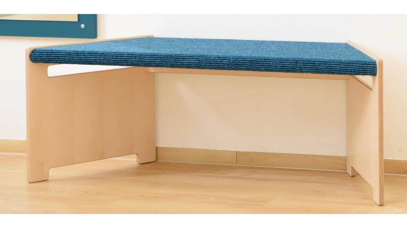 Trapezbank met blauw Tretford-tapijt en handgreepgaten voor eenvoudig verplaatsen, op houten basis.