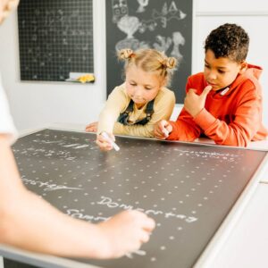 Kinderen schrijven op een bewegend bord, met een focus op samenwerking en leren door beweging.