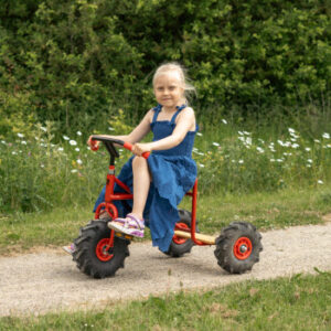 ROSE kinderdriewieler met tractorbanden, metalen frame en houten zitting, gebruikt door een meisje op een pad.