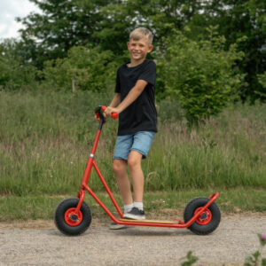 Roze step met ballonbanden, gebogen stuur en stabiele basis, gebruikt door een lachende jongen in een groene omgeving.