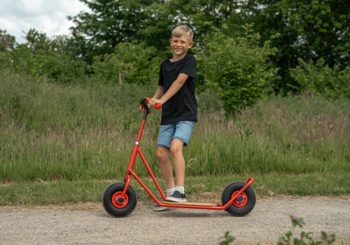 Roze step met ballonbanden, gebogen stuur en stabiele basis, gebruikt door een lachende jongen in een groene omgeving.