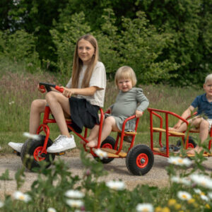 ROSE kinderdriewieler met passagierszitje en ballonbanden, kinderen rijden op een pad omringd door bloemen.
