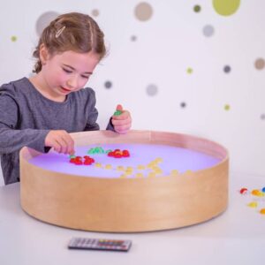 Ronde lichttafel met 16 kleuren, diameter 50cm, hoogte 12cm; meisje speelt met kleurrijke objecten op de tafel.