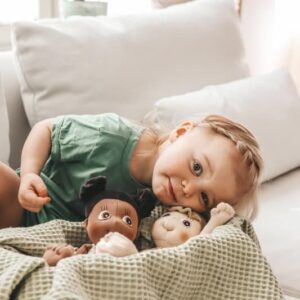 Zachte, handgemaakte Familie Rubens poppen in een mand, met een kind dat ernaast ligt op een bank.