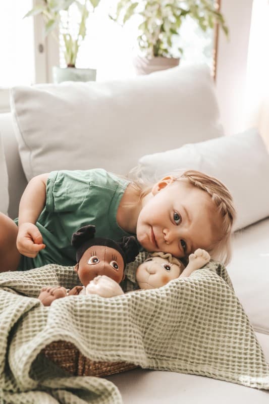 Zachte, handgemaakte Familie Rubens poppen in een mand, met een kind dat ernaast ligt op een bank.